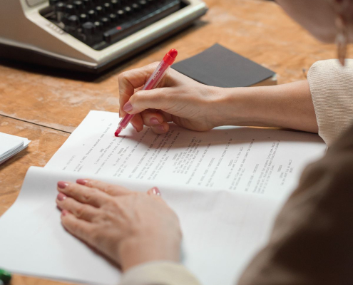 A writer edits a manuscript with a red pen beside a vintage typewriter