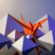 An orange origami crane standing out from a crowd of identical folded paper shapes