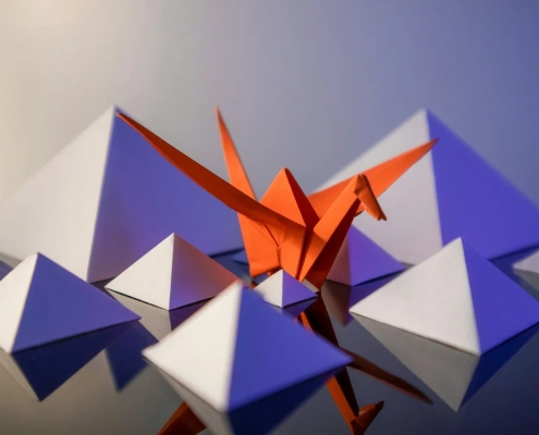 An orange origami crane standing out from a crowd of identical folded paper shapes