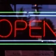 Red neon open sign glowing in a dark shop window at night