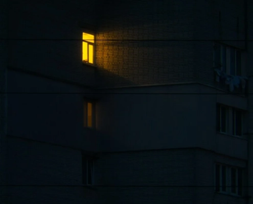 A single lit window glowing amber in a dark apartment building at night