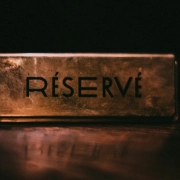 A brass plate engraved RÉSERVÉ on a dark polished table, lit from one side