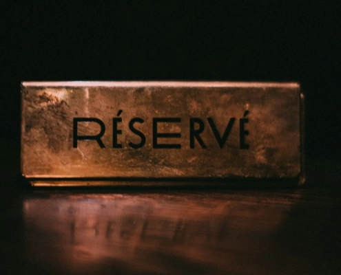 A brass plate engraved RÉSERVÉ on a dark polished table, lit from one side