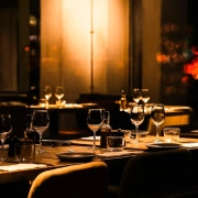 A dimly lit restaurant table laid with glasses and plates, chairs empty, warm light in a dark room
