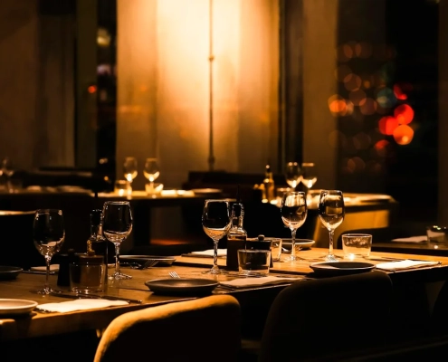 A dimly lit restaurant table laid with glasses and plates, chairs empty, warm light in a dark room